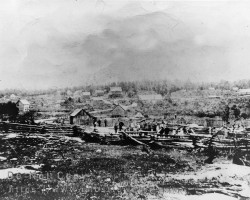 An early town view of Seguin Falls with a large group of people clustered along the Nipissing Road. The King George Hotel can be seen in the background. ca. early 1900s Town view